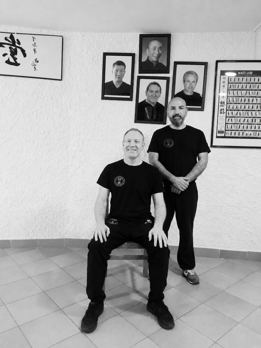 Sifu Antonio Bacino seduto e Riccardo Geraci in piedi, sotto i ritratti dei maestri della linea